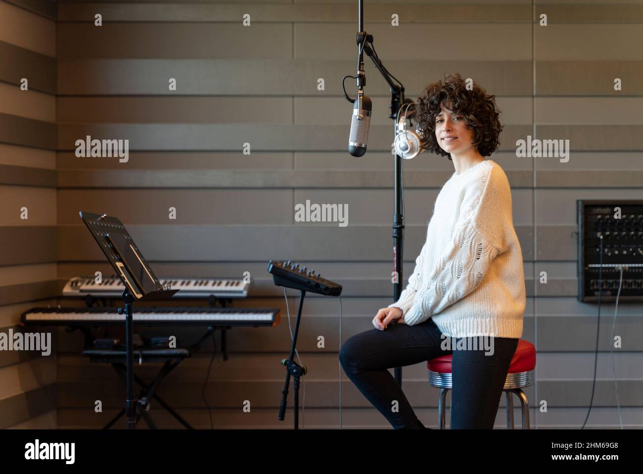 Eine junge Sängerin mit lockigen Haaren, die in einem echten Studio einen Song aufzeichnete. Stockfoto
