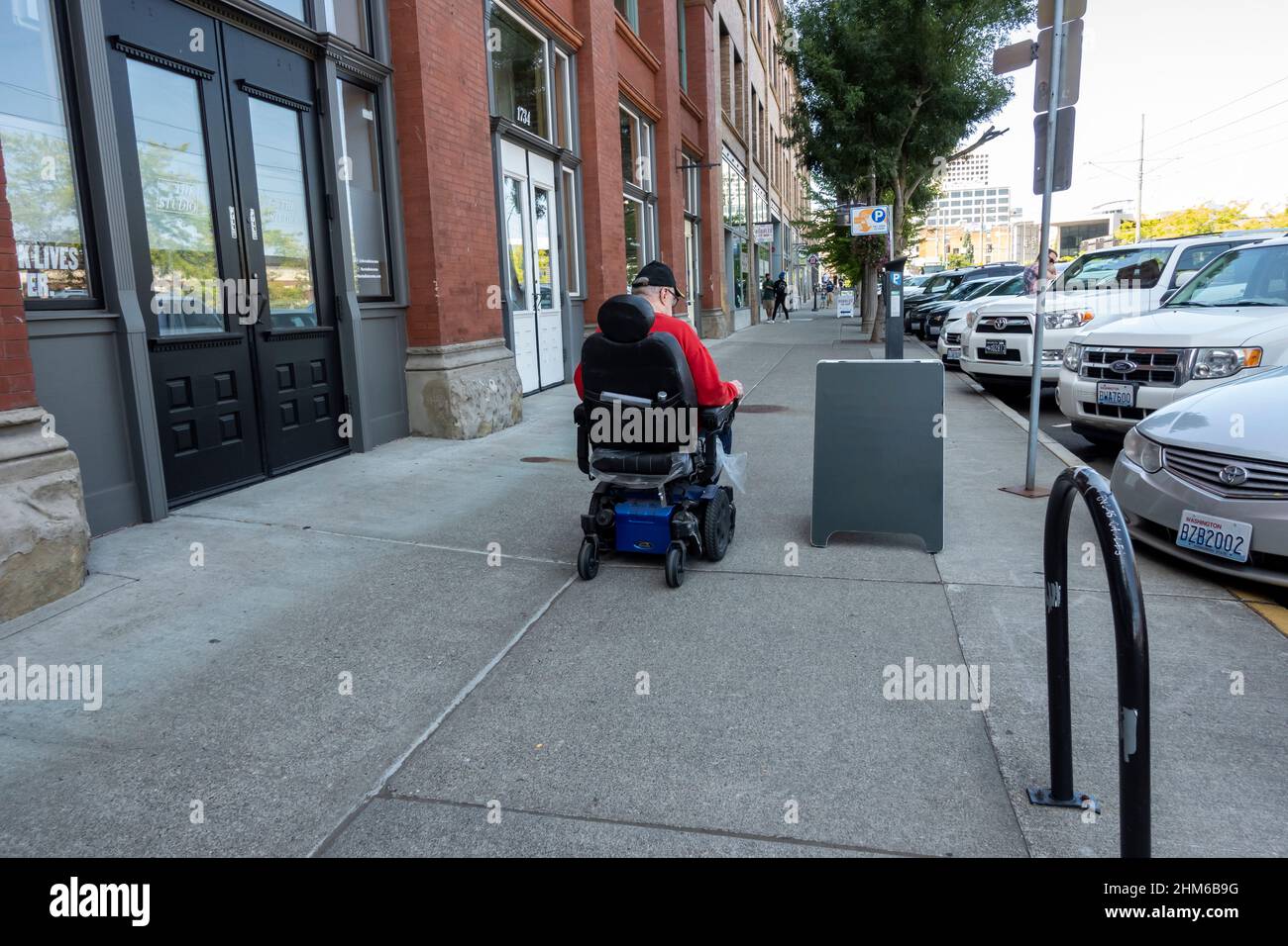 Tacoma, WA USA - ca. August 2021: Mann mittleren Alters in einem motorisierten Rollstuhl, der den Bürgersteig in der Innenstadt entlang geht. Stockfoto