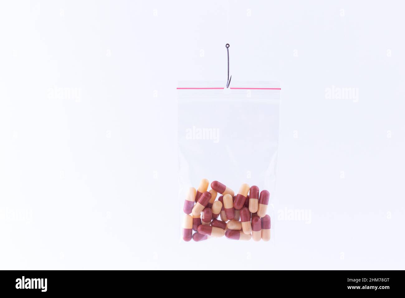 Die pharmazeutische Falle und Drogensucht - farbige Pillen oder Tabletten, die in einem kleinen Ziplock-Beutel auf einem Angelhaken gegen den weißen Hintergrund hängen Stockfoto