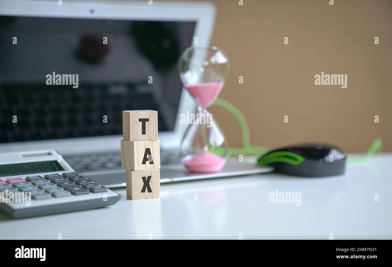 Das Wort Steuer auf Holzwürfel, neben Computer-Laptop, Rechner und Sanduhr. Konzept der Steueranmeldung. Stockfoto
