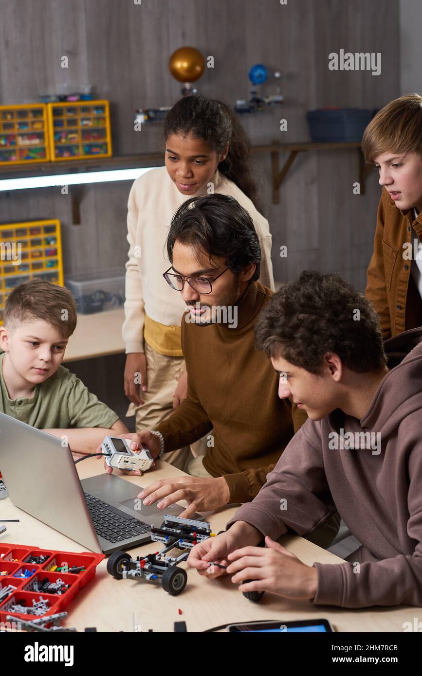 Vertikales Porträt eines jungen männlichen Lehrers mit einer vielfältigen Gruppe von Kindern im Robotikunterricht in der Schule Stockfoto
