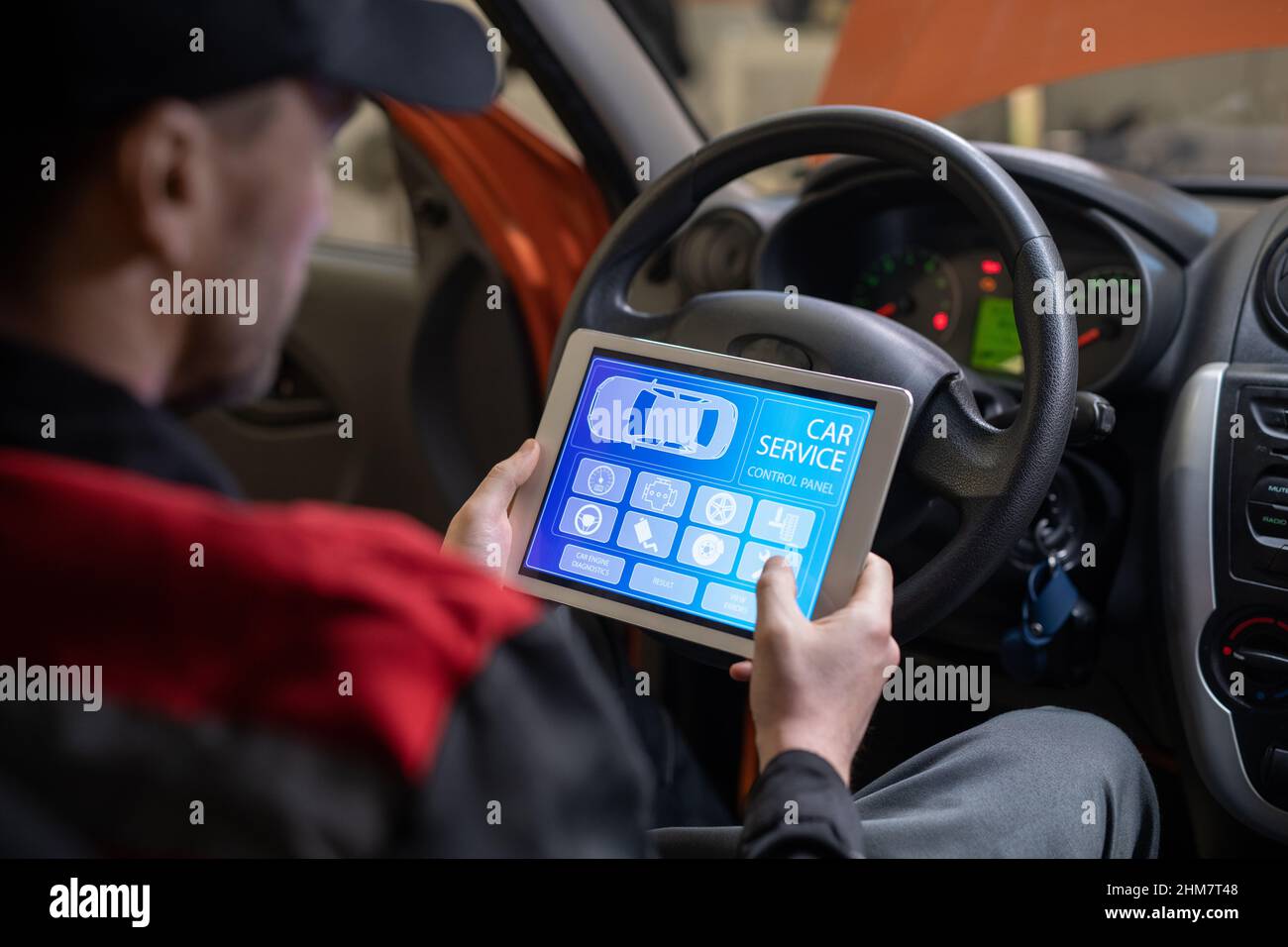 Nahaufnahme des Kfz-Mechanikers mit digitalem Tablet mit Service- und Wartungs-App auf dem Bildschirm, während das Fahrzeug in der Autowerkstatt inspiziert wird Stockfoto