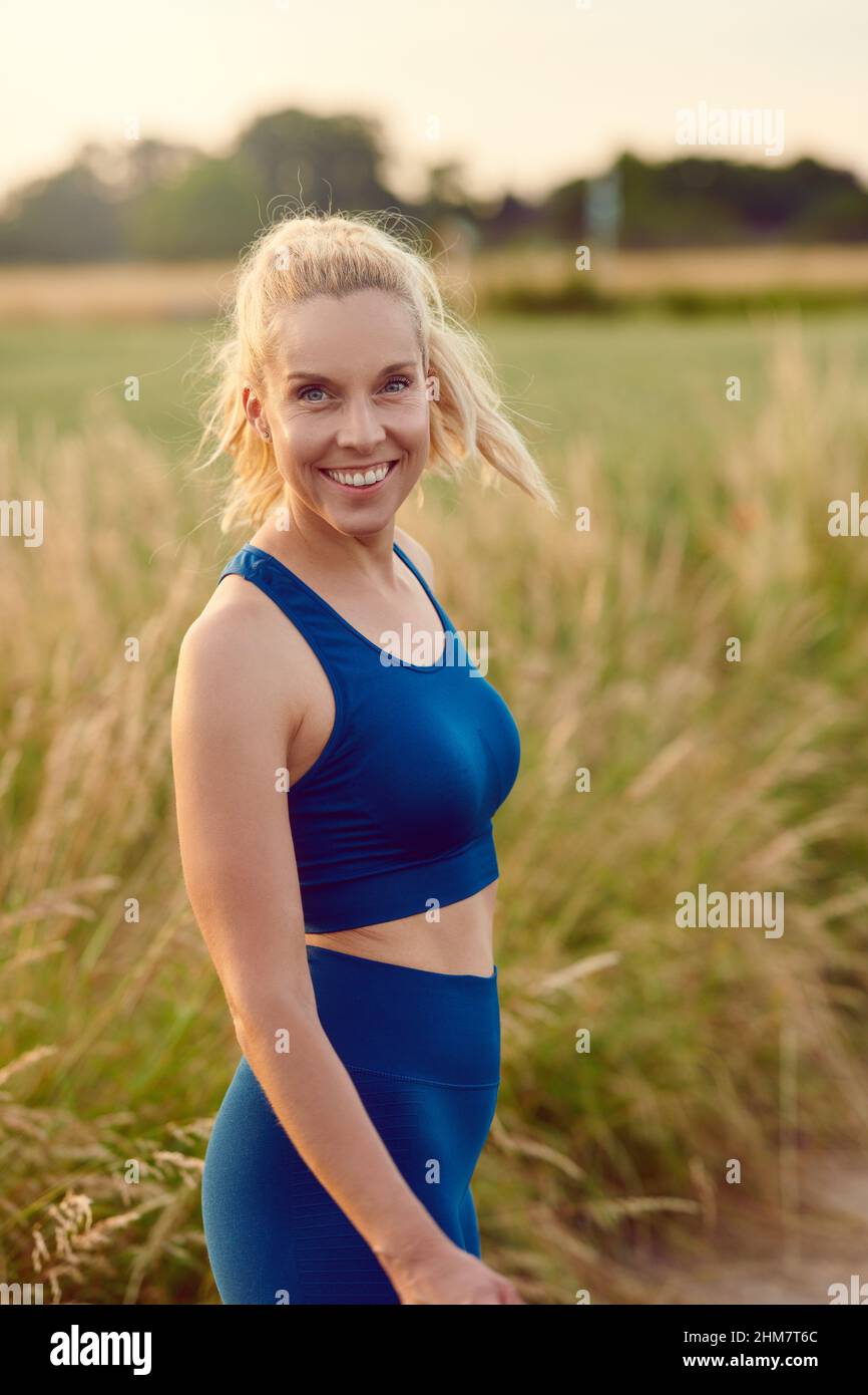 Eine attraktive, gesunde Frau, die sich an der Kamera lächelt, während sie sich darauf vorbereitet, in einem gesunden, aktiven Outdoor-LIF auf einem ländlichen Wanderweg zu joggen Stockfoto