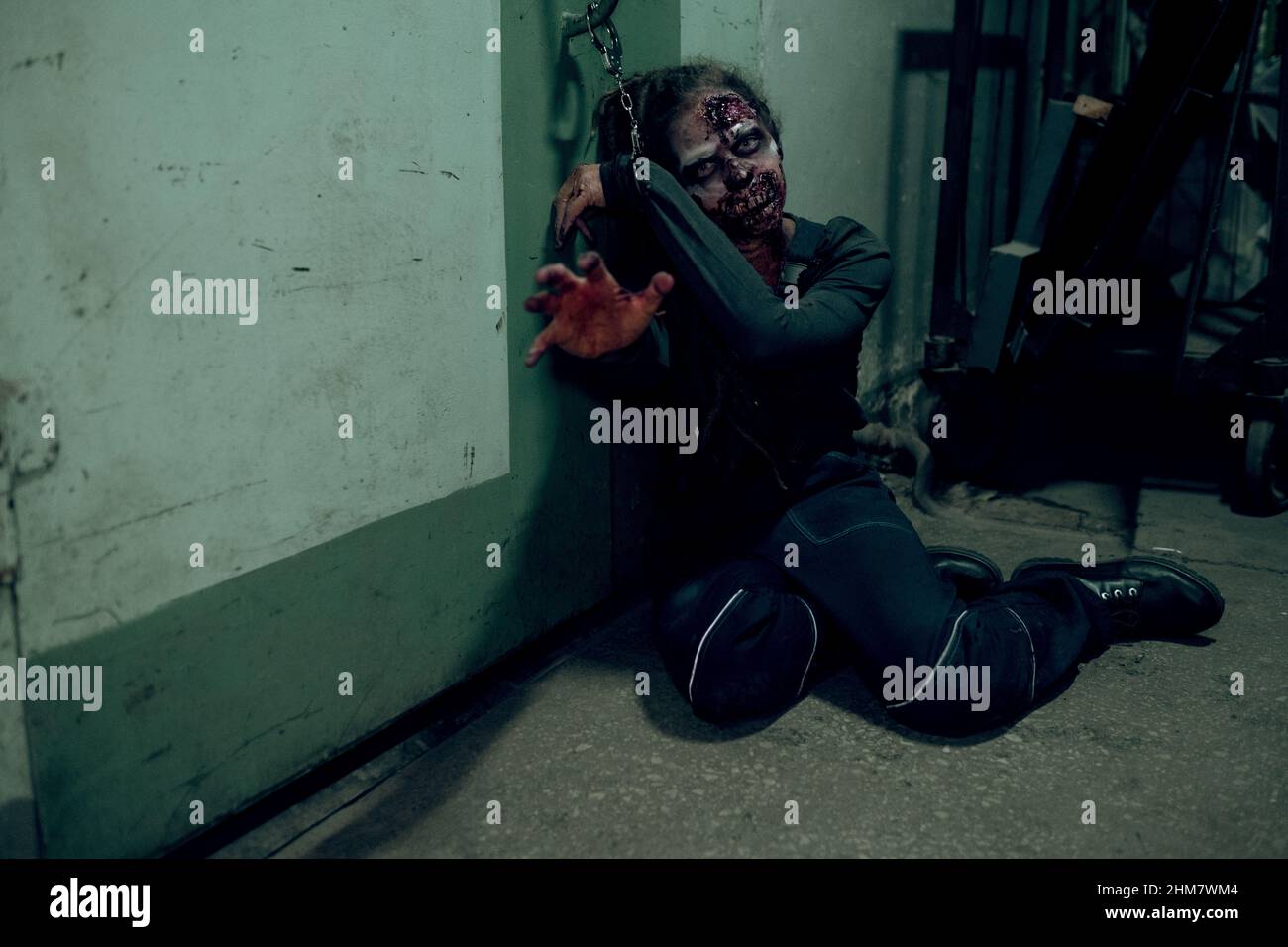 Ganzkörperaufnahme eines weiblichen Zombies, der im dunklen Raum an die Wand gekettet ist und bis zur Kamera reicht, Raum kopieren Stockfoto