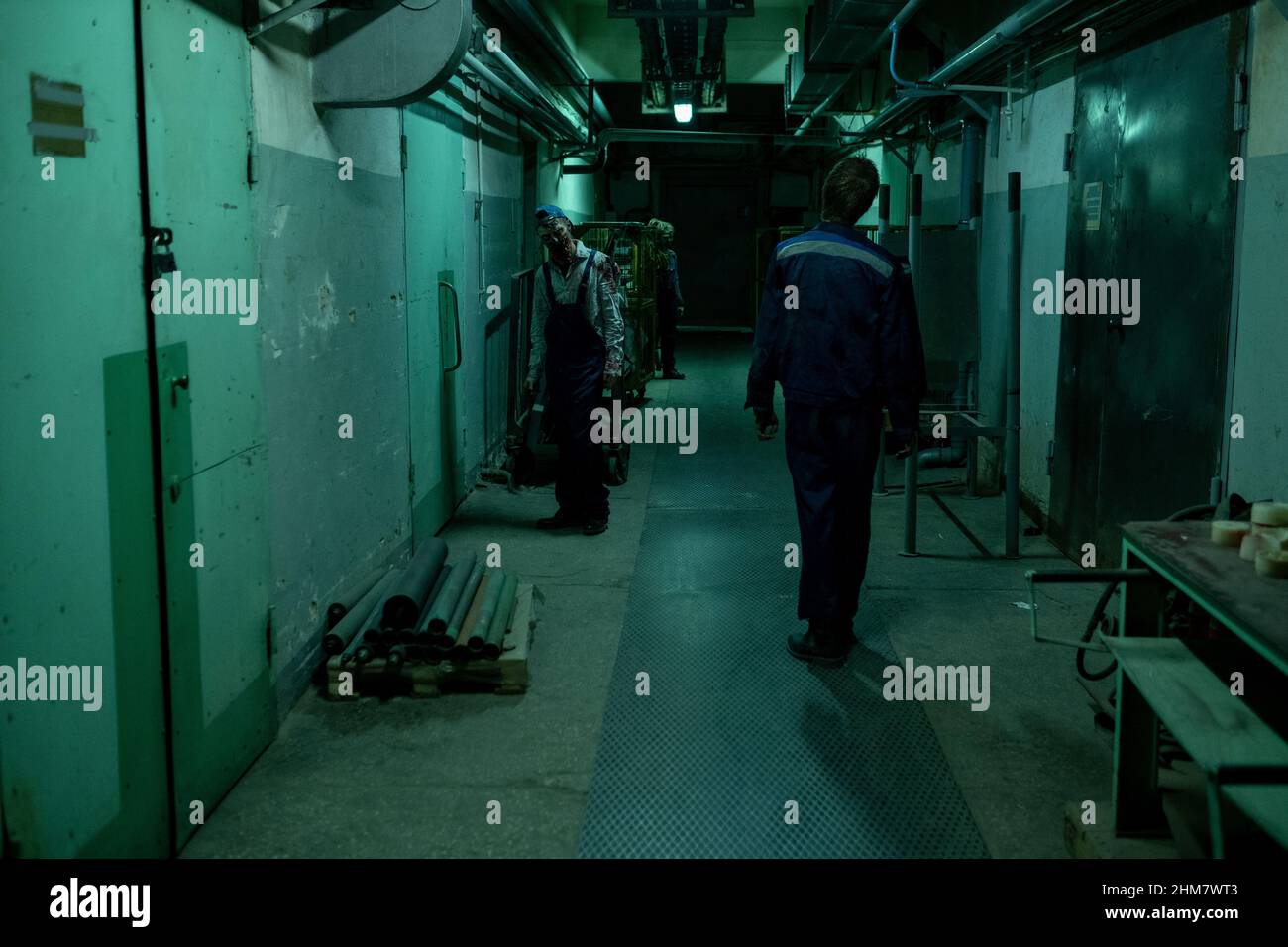 Weitwinkelansicht von Zombies, die in einem dunklen Industrieflur durch gruseliges grünes Licht gehen, Kopierraum Stockfoto
