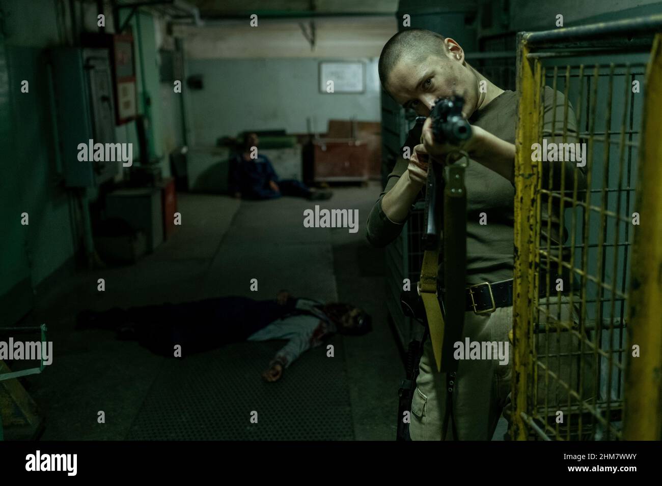 Waist-up-Porträt einer harten Soldatin, die im dunklen Industrieflur mit Zombies im Hintergrund auf die Kamera zeigt, Kopierraum Stockfoto