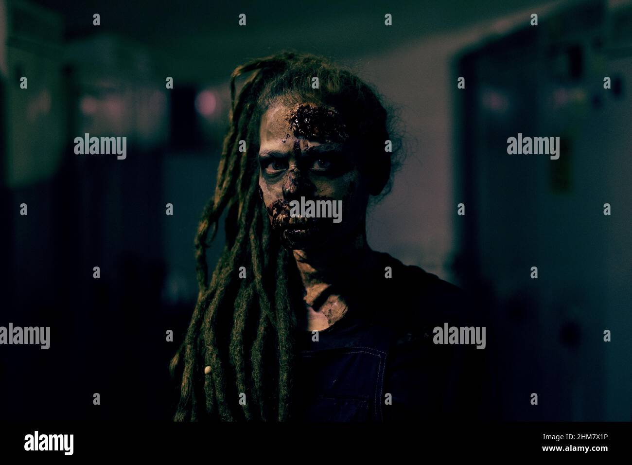 Frontansicht einer jungen Frau, die ein Zombie FX Make-up trägt und die Kamera im dunklen Raum ansieht, Kopierraum Stockfoto