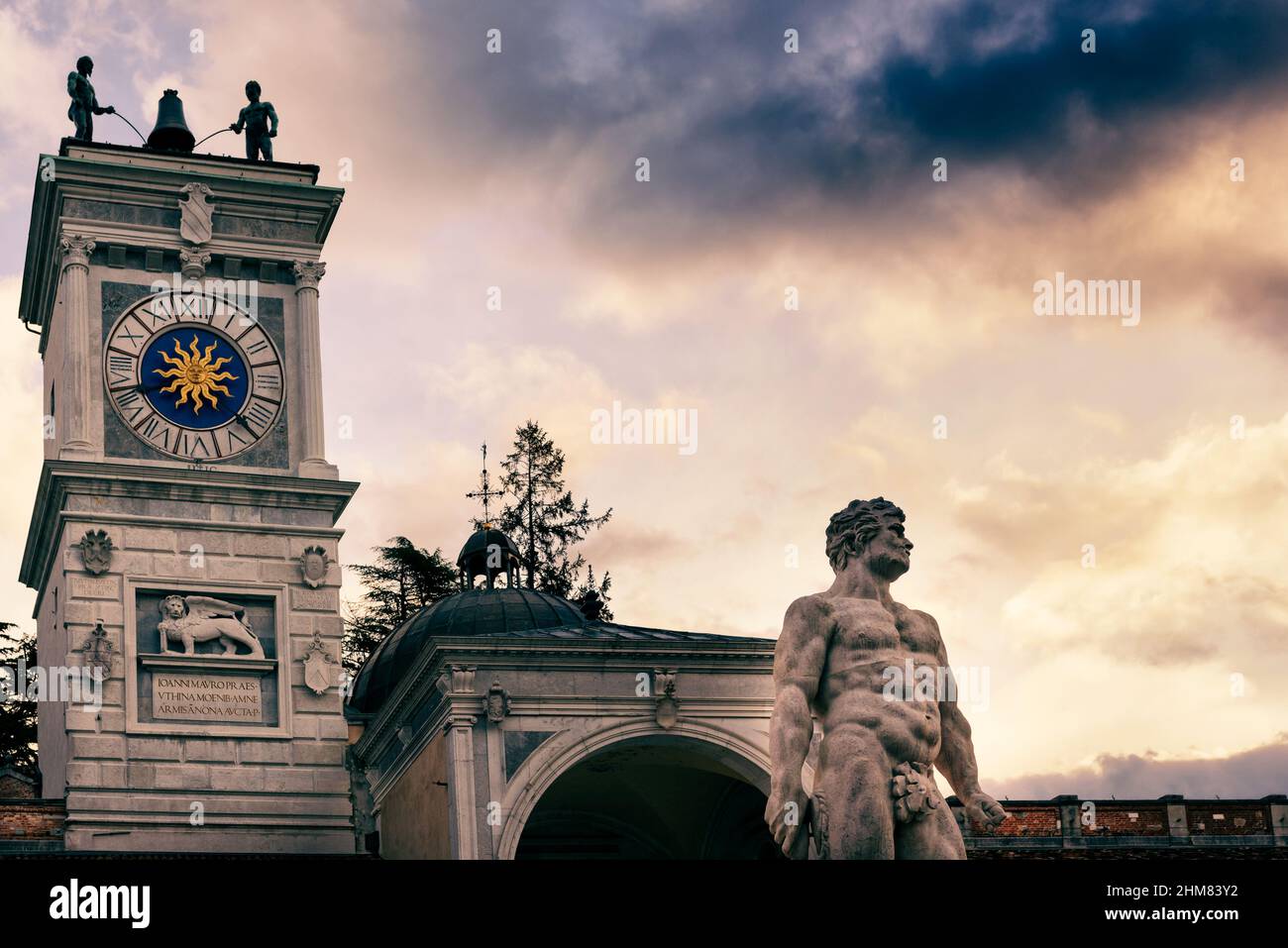 Herkules-Statue mit Uhrenturm im Hintergrund. Italienische klassische Kunst und Architektur unter einem schönen Himmel. Udine, Friaul Julisch Venetien, Italien. Stockfoto