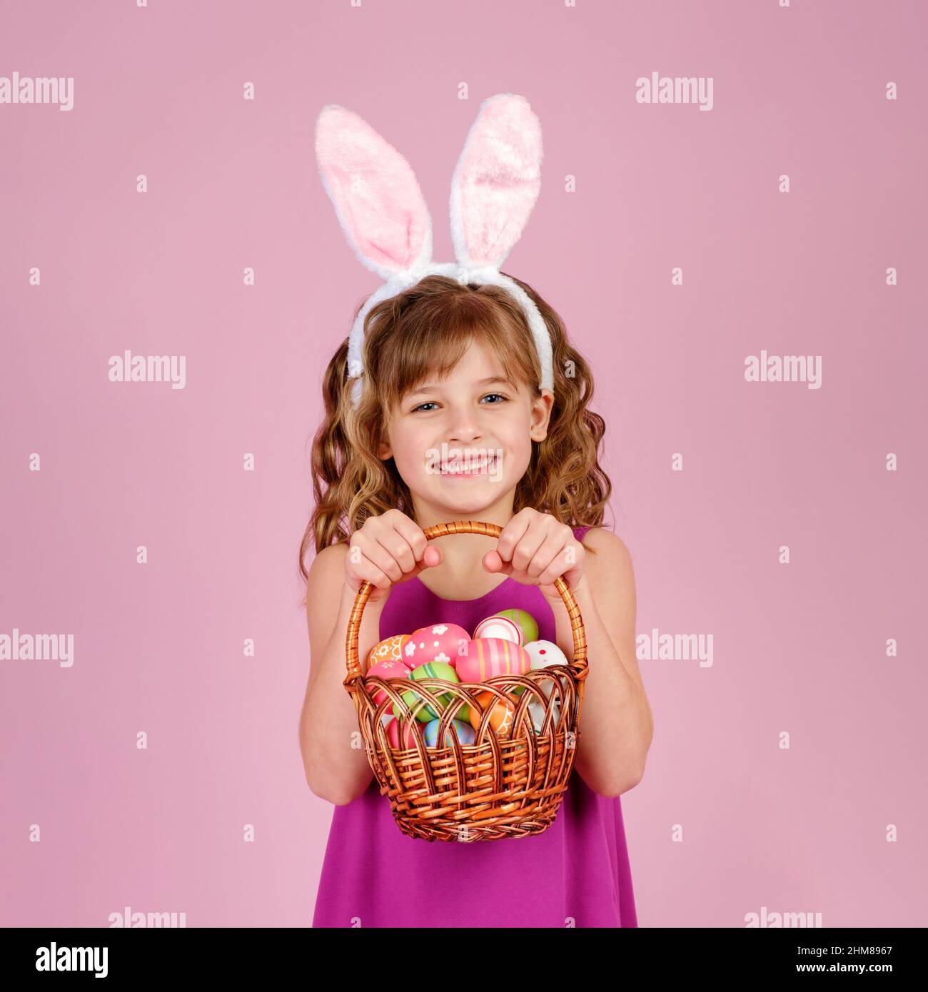 Fröhliches Kind hält Korb mit Ostereiern in rosa Studio Stockfoto