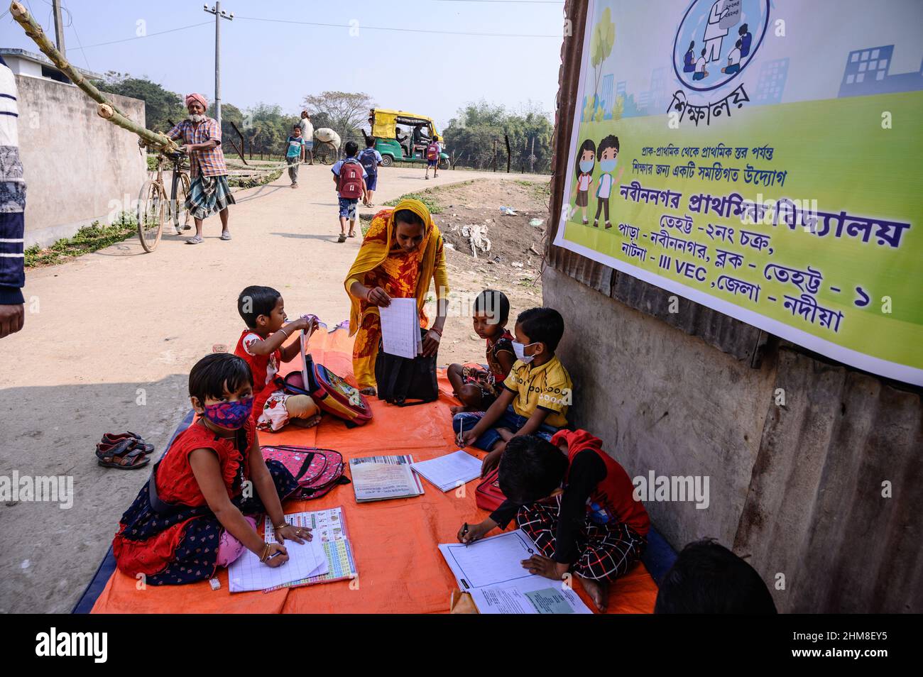 Nabin Nagar, Westbengalen, Indien. 7th. Februar 2022. Die Regierung des Bundesstaates Westbengalen hat am 7th. Februar „˜Paray Shikshalaya“ ins Leben gerufen, Eine gemeindebasierte Schularbeit in Nachbarschaften, die sich an Grundschüler richtet, um die programmierten Ziele zu erreichen, besteht darin, einen großen Teil der Schüler zurückzuholen, die in den letzten zwei Jahren aufgrund der Schließung von Schulen aufgrund von Covid-19 aus dem formalen Bildungssystem ausgefallen sind. Die Vorschulklasse einer an der Grenze zwischen Indien und Bangladesch angrenzenden Grundschule wird auf einer leeren Straße neben dem Zaun bei Nabin Nagar durchgeführt, es kommen gelegentlich Haustiere. (Kredit Stockfoto