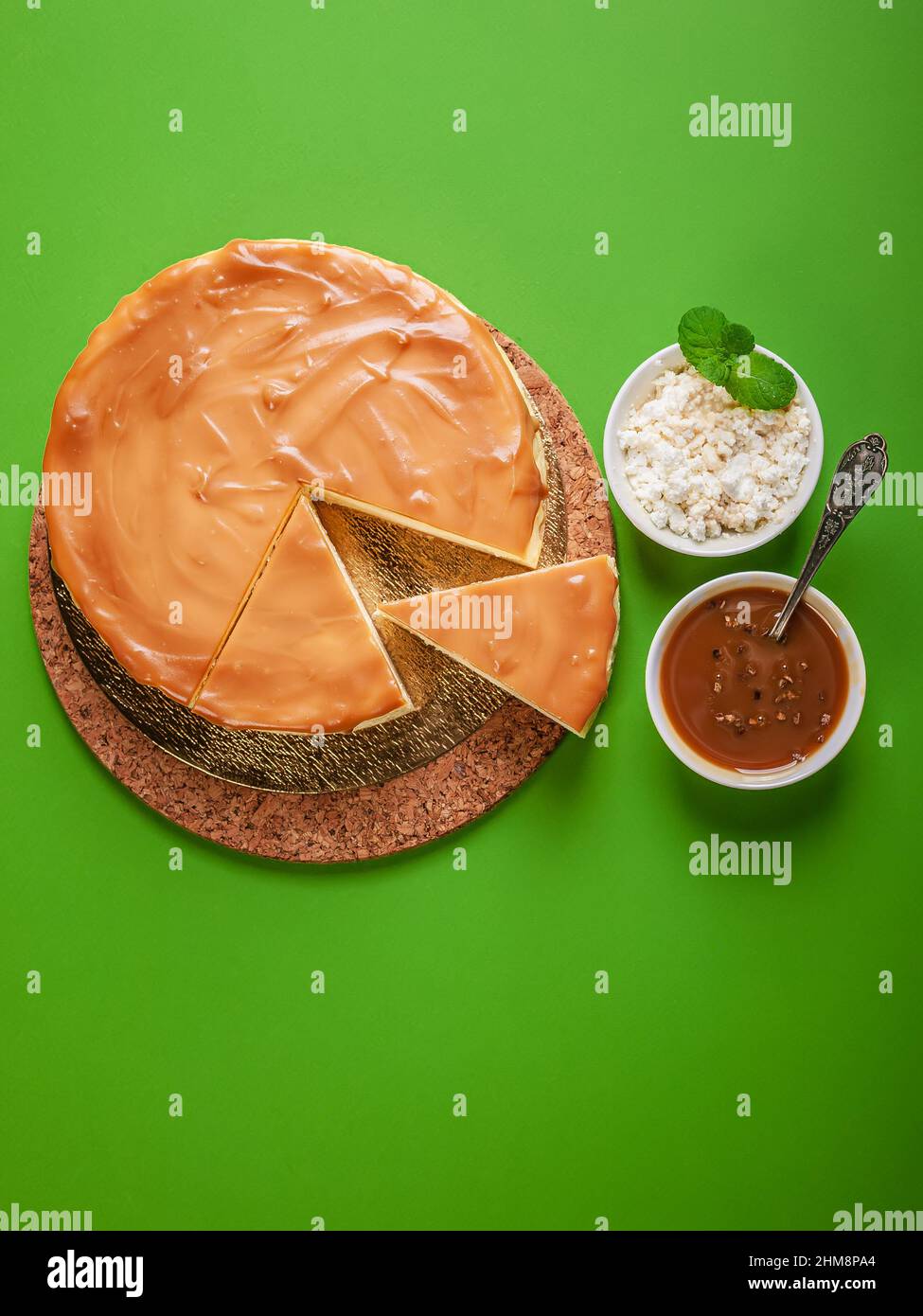 Klassischer Käsekuchen mit gesalzenem Karamell auf grünem Hintergrund. Hausgemachtes, köstliches Gebäck. Süßes Dessert. Vertikale Aufnahme. Speicherplatz kopieren Stockfoto