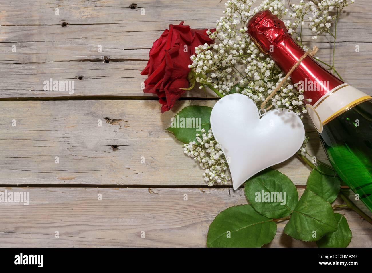 Weißes Herz, Champagnerflasche und eine rote Rose auf einem rustikalen Holztisch, romantisches Liebeskonzept zum Valentinstag, Mutter- oder Vatertag, Raum kopieren, zu Stockfoto