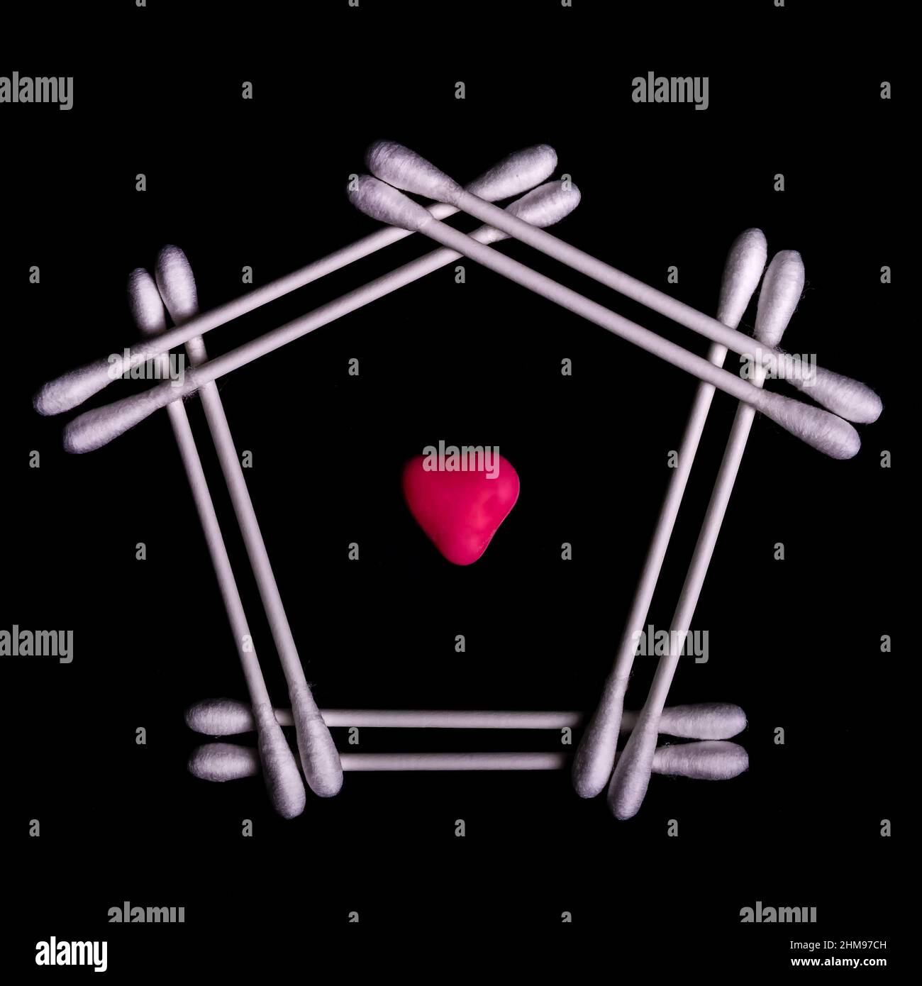 Einige Wattestäbchen sind auf einer glänzenden schwarzen Oberfläche mit der Form eines Hauses und einem roten Herz in der Mitte angeordnet Stockfoto