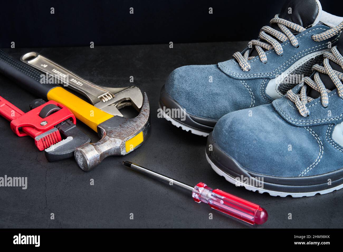 Sicherheitsschuhe, Hammer, Schraubendreher und Schraubenschlüssel auf schwarzem Hintergrund Stockfoto