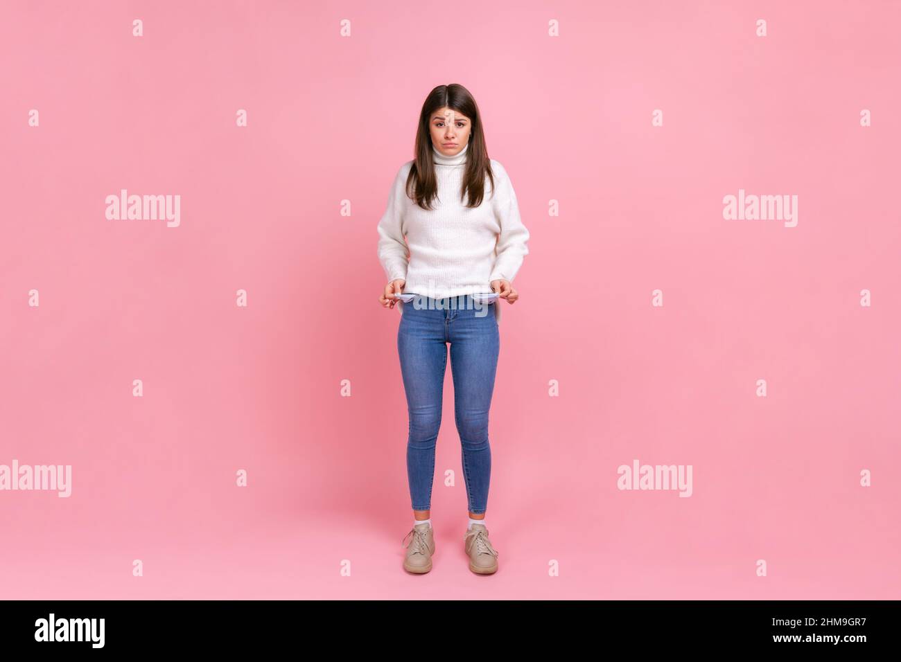 In voller Länge Porträt des Mädchens zeigt leere Taschen und suchen frustriert über Darlehen und Schulden, trägt weißen lässigen Stil Pullover. Innenaufnahme des Studios isoliert auf rosa Hintergrund. Stockfoto