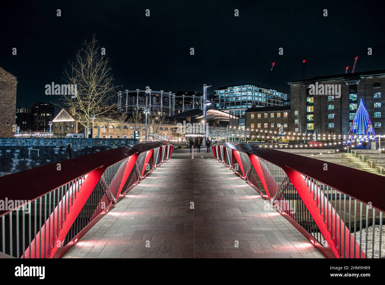 Brücke über den Regent's Canal, die zum Granary Square, Coal Drops Yard führt, alle nachts beleuchtet. Die Entwicklung der Gasinhaber ist im Hintergrund zu sehen. Stockfoto