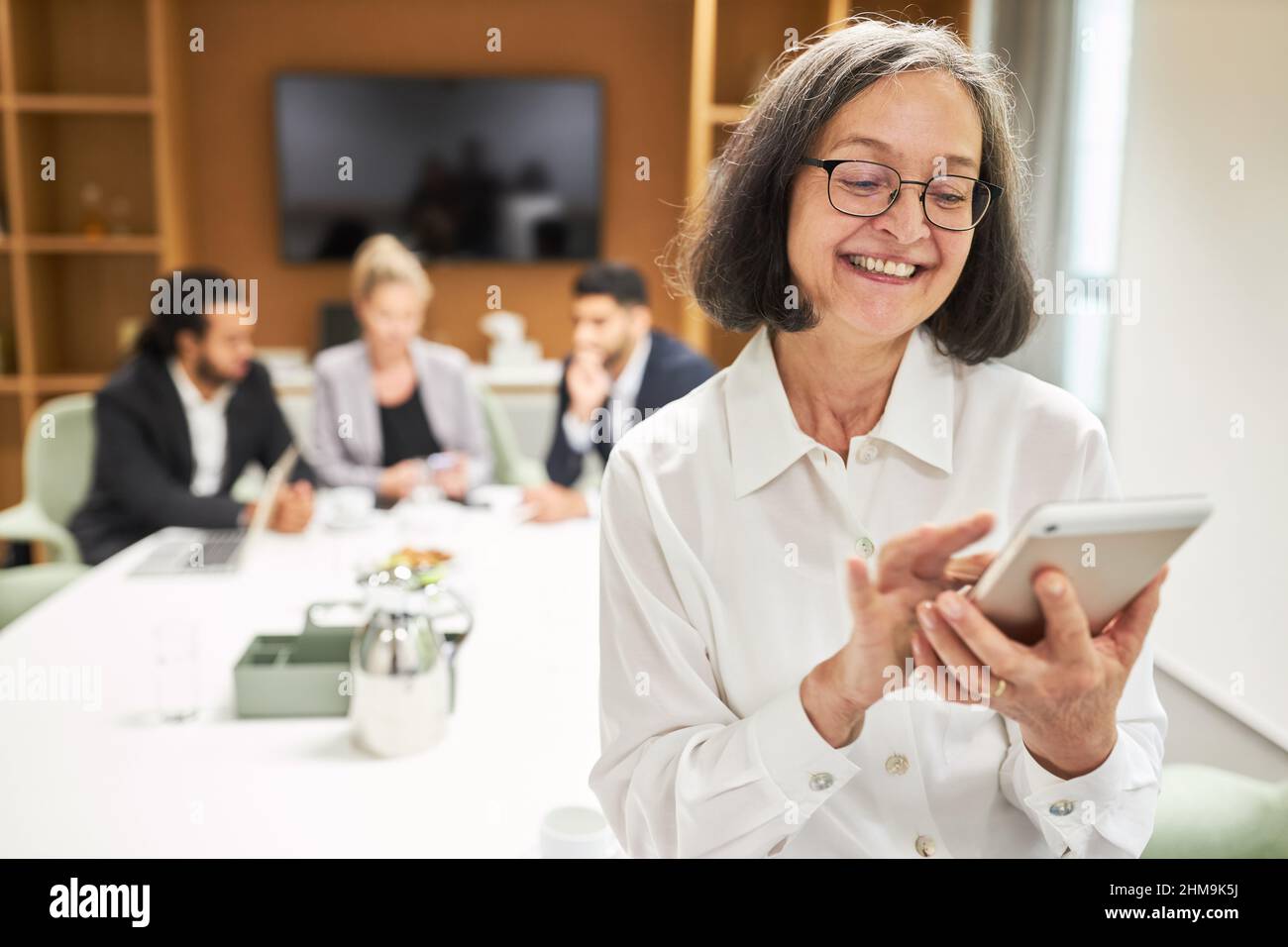 Glückliche Geschäftsfrau, die bei einem Geschäftstreffen im Büro eine sms-Nachricht auf das Smartphone schreibt Stockfoto