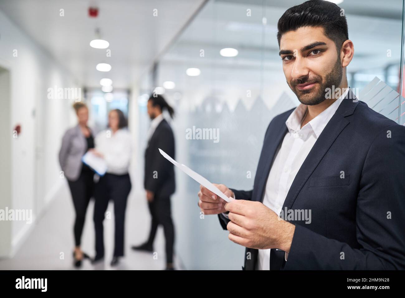 Junger Mann als Auszubildender oder Bewerber mit einem Arbeitsvertrag oder einer Bescheinigung im Flur des Büros Stockfoto