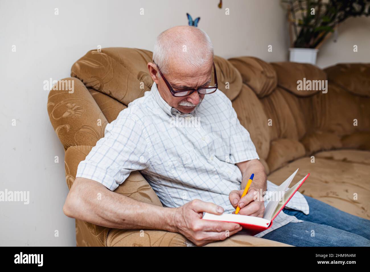 Ein älterer Mann notiert sich in einem Notizbuch, nachdem er Rechnungen bezahlt hat. Rentner macht die alte Buchführung, indem er Notizen in einem Buch mit dickem Einband macht. Stockfoto