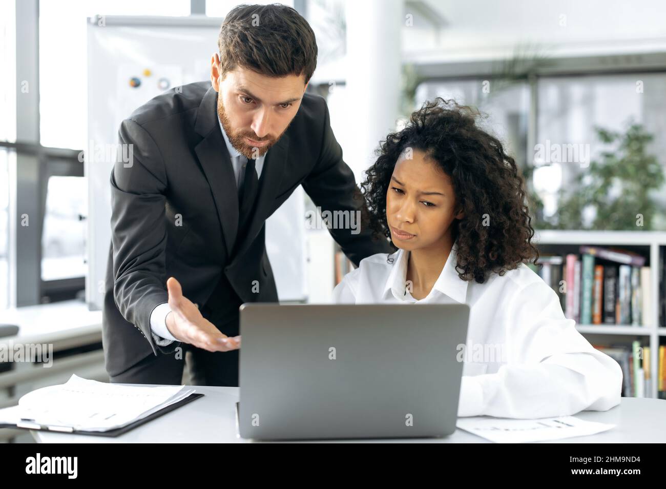 Erfolgreiche, multirassische Kollegen aus dem Geschäft, afroamerikanische Frau und kaukasischer Mann, sitzen am Schreibtisch im modernen Büro, nutzen Laptop, diskutieren neues Projekt, planen Geschäftsstrategie Stockfoto