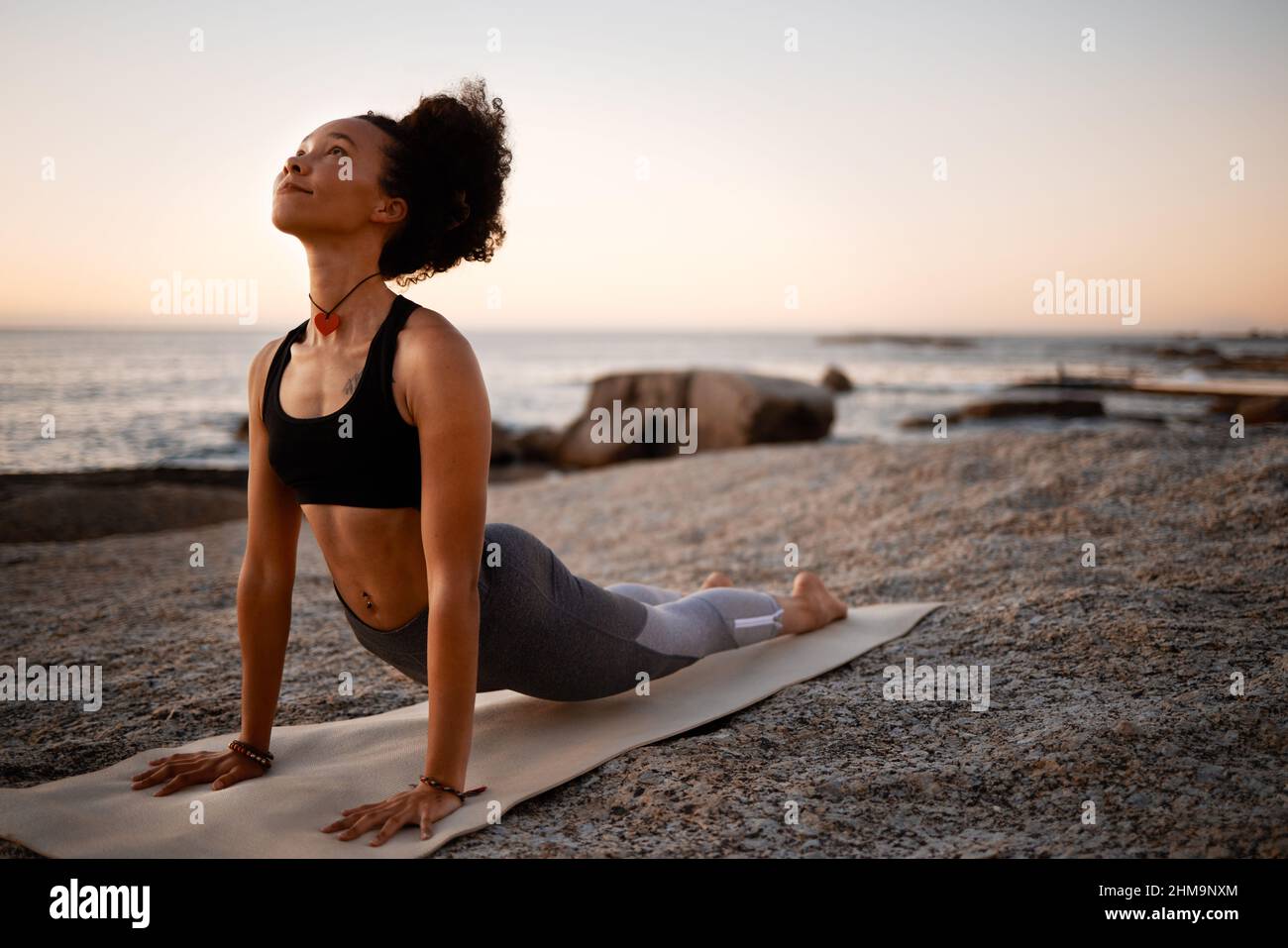 Der Himmel hält alle Antworten bereit. Ganzkörperaufnahme einer attraktiven jungen Frau, die am Strand bei Sonnenuntergang Yoga praktiziert. Stockfoto