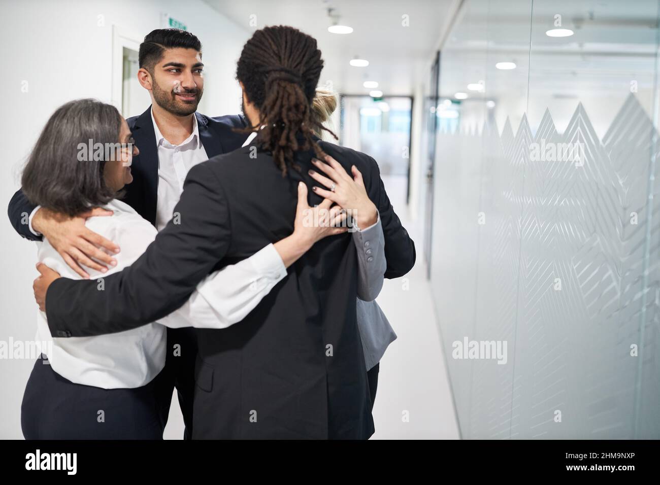 Die Mitarbeiter des Geschäftsteams im Büroflur stehen in einem Kreis, der sich für Teambildung und Zweisamkeit umarmt Stockfoto