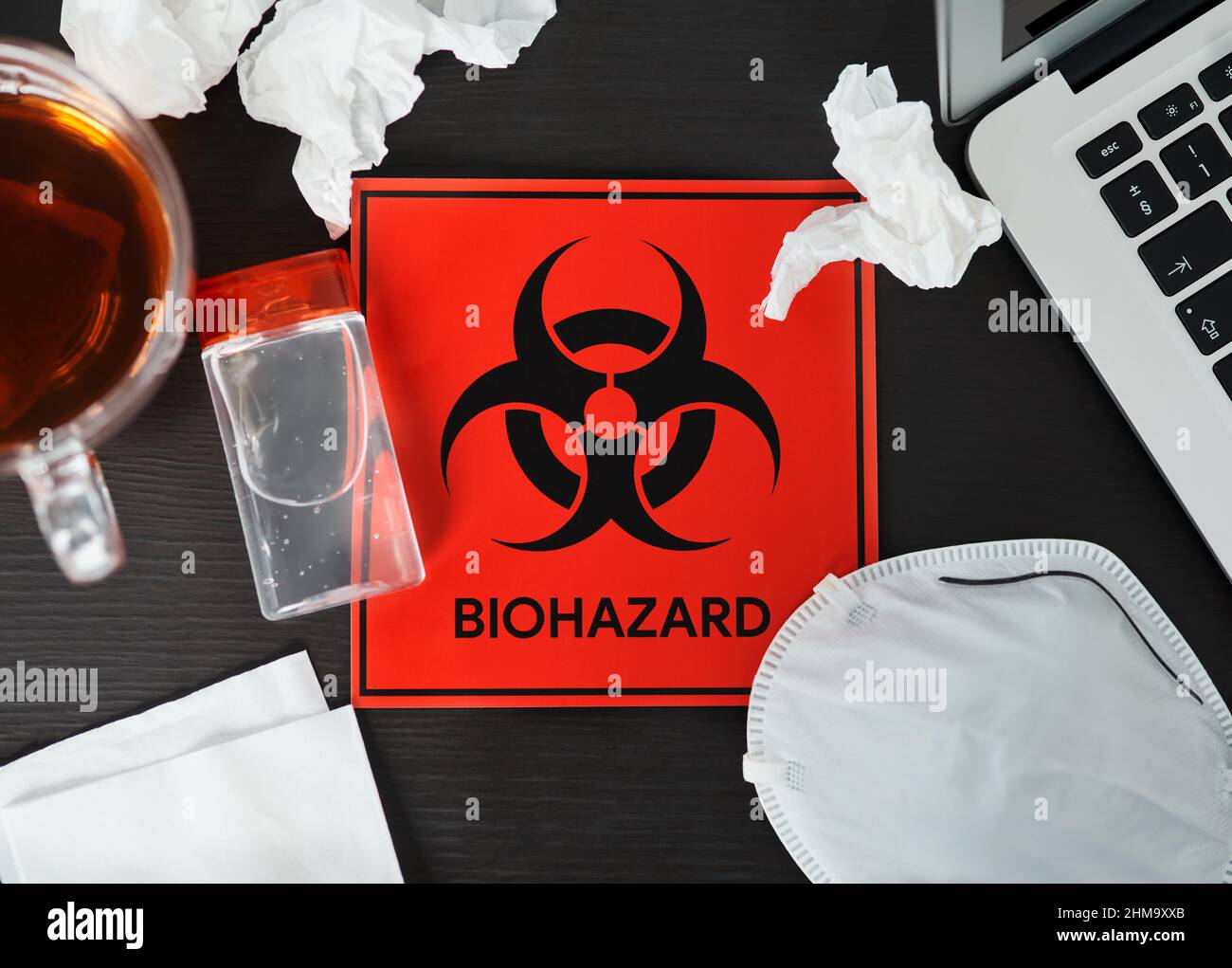 Bleiben Sie zu Hause, um zu verhindern, dass sich Ihre Kollegen infizieren. Aufnahme eines Schildes für biologische Gefahren auf einem Arbeitsplatz. Stockfoto