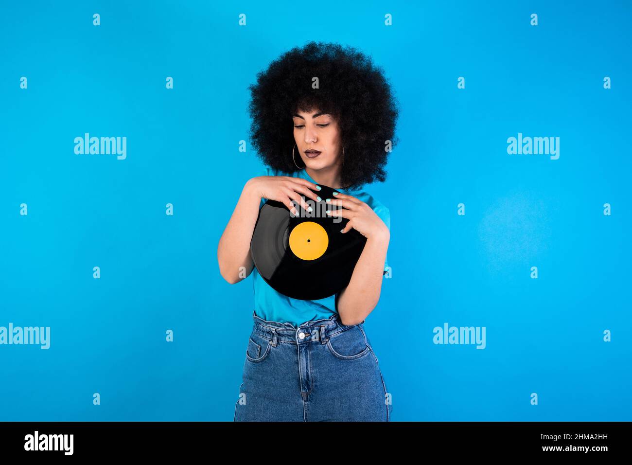 Unemotionale hispanische Meloman mit Retro-Vinyl-Platte, die im Light Studio auf blauen Hintergrund schaut Stockfoto