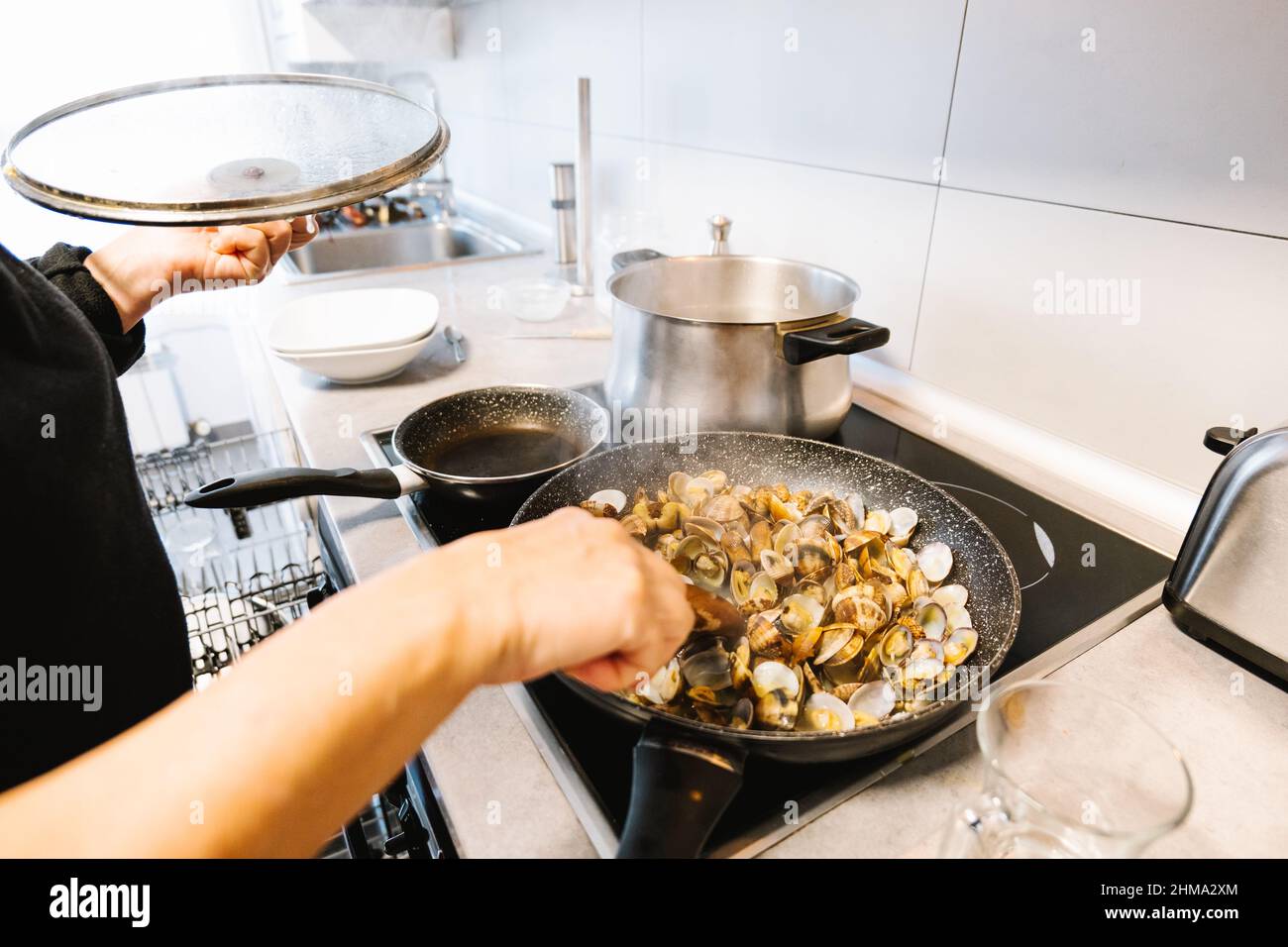 Eine Menge leckerer Weichtiere mit Muscheln, die in einer heißen schwarzen Bratpfanne auf einem Elektroherd in der hellen Küche zu Hause braten Stockfoto