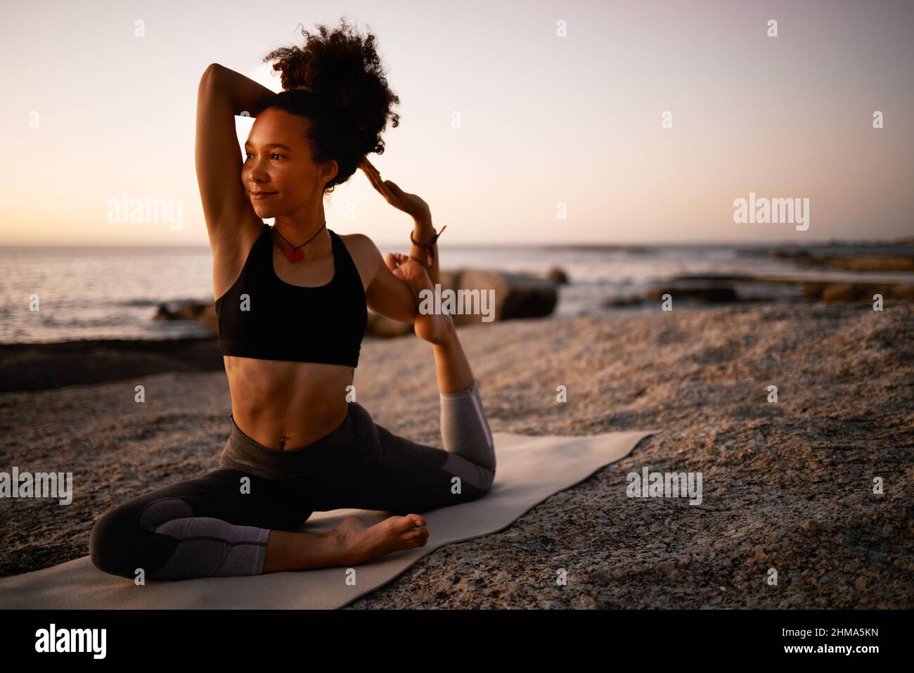 Yoga ist der perfekte Weg, um limber zu bleiben. Ganzkörperaufnahme einer attraktiven jungen Frau, die am Strand bei Sonnenuntergang Yoga praktiziert. Stockfoto