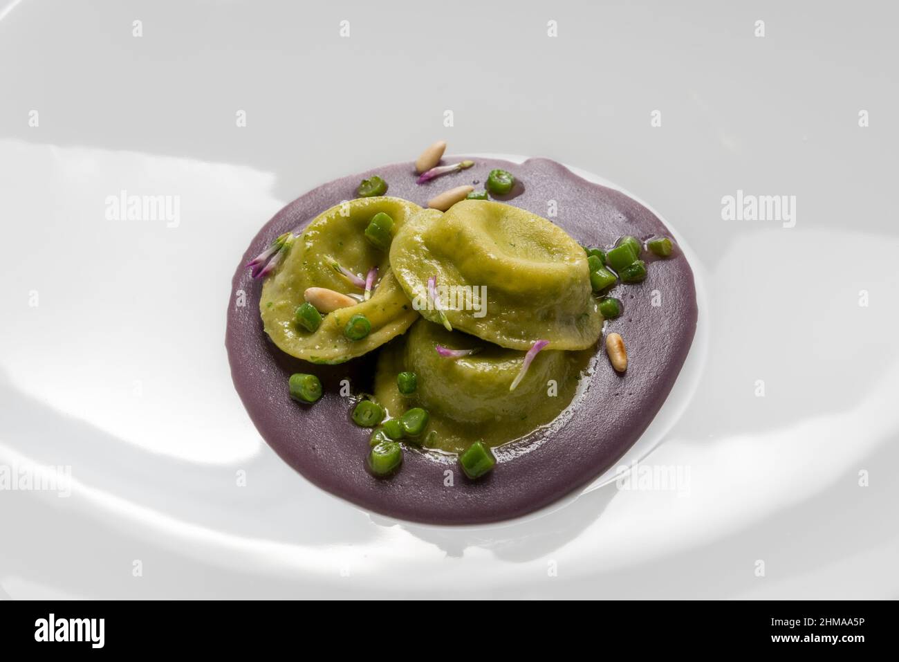 Grüner Spinat Tortelloni gefüllt mit Käse und Gemüse, auf Rote Bete Püree mit Erbsen und Pinienkernen, Nahaufnahme Stockfoto