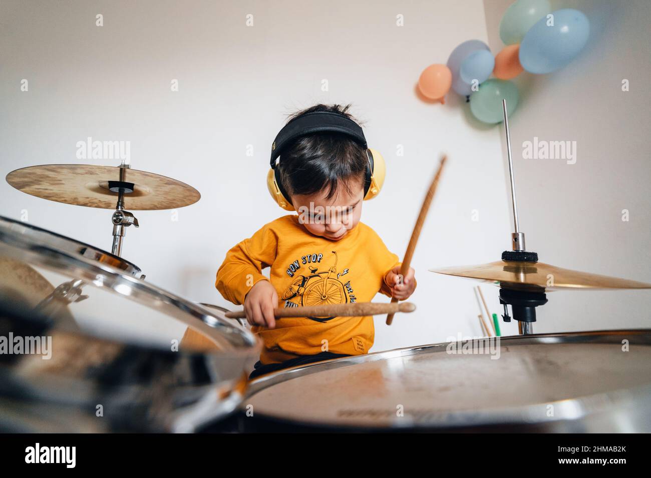 Motivierter Junge, der mit geräuschisolierenden Kopfhörern Schlagzeug spielt Stockfoto