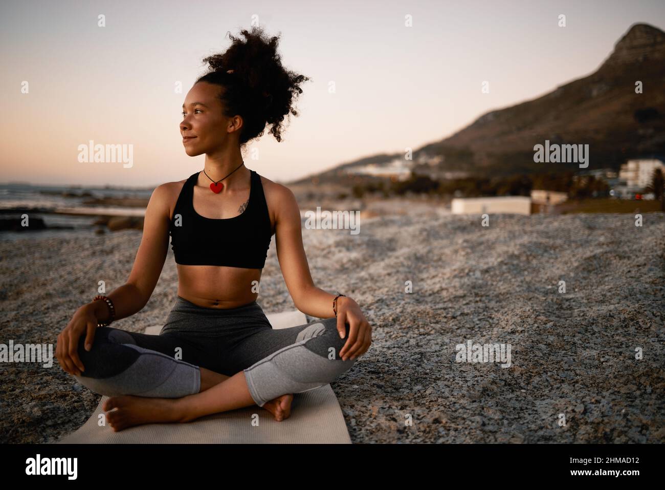 Es ist der perfekte Ort für Yoga. Ganzkörperaufnahme einer attraktiven jungen Frau, die am Strand bei Sonnenuntergang Yoga praktiziert. Stockfoto