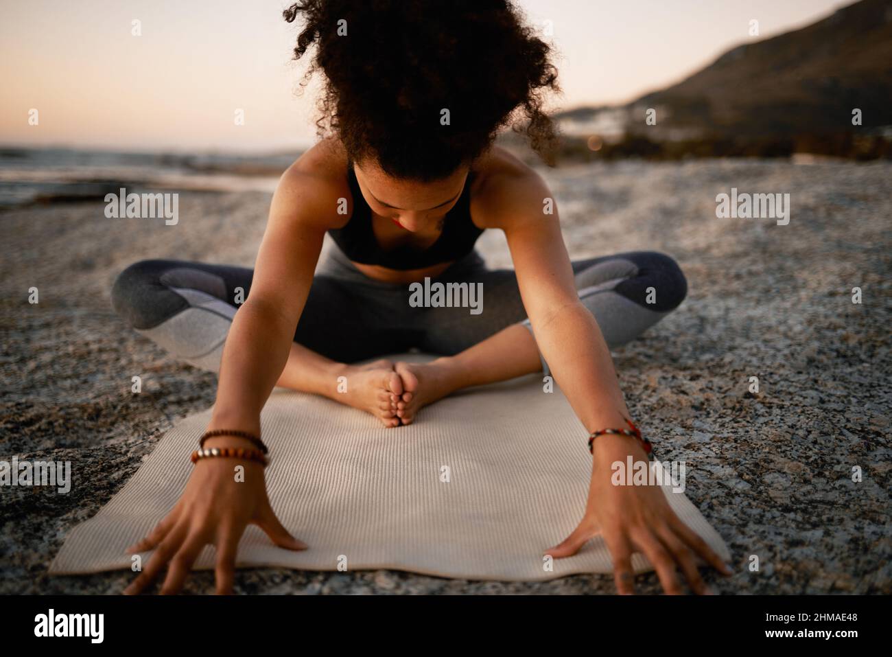Lockern Sie Ihren Körper, befreien Sie Ihren Geist. Ganzkörperaufnahme einer attraktiven jungen Frau, die am Strand bei Sonnenuntergang Yoga praktiziert. Stockfoto
