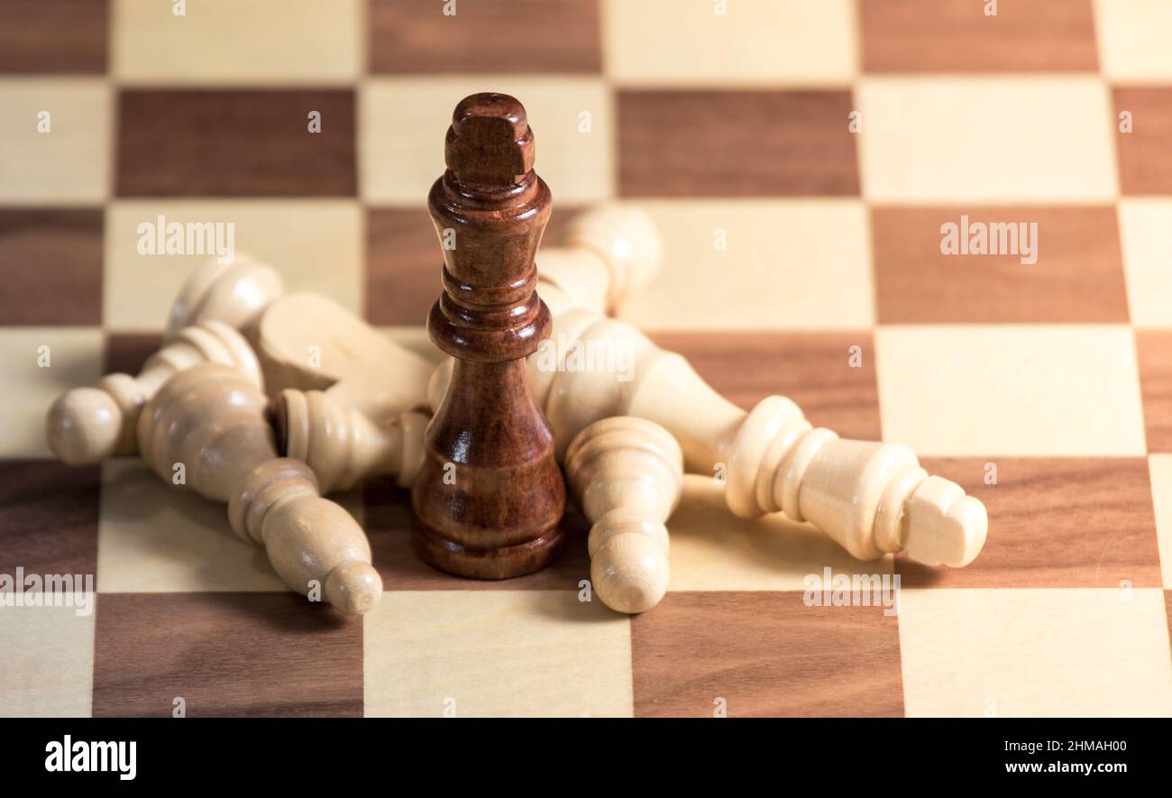 Gefallene Schachfiguren, die um einen König auf einem Schachbrett liegen. Licht scheint von der rechten Seite Stockfoto