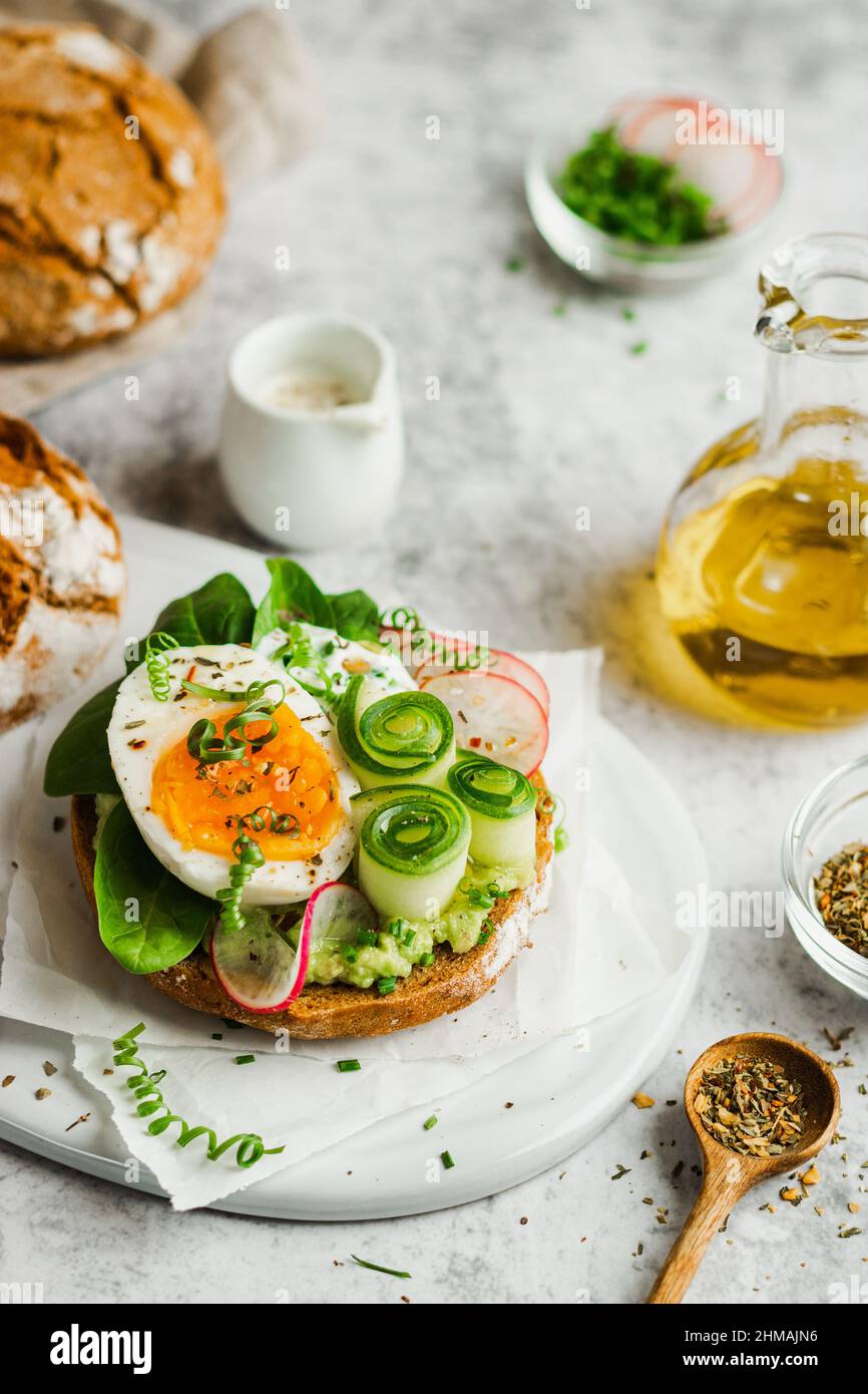 Gesundes, natürliches Sommerfutter. Serviert Sandwiches mit Vollkornbrot, Avocado, Eiern, Rettich, Gurke auf weißem Brett und weißem Hintergrund. Mittagessen Stockfoto