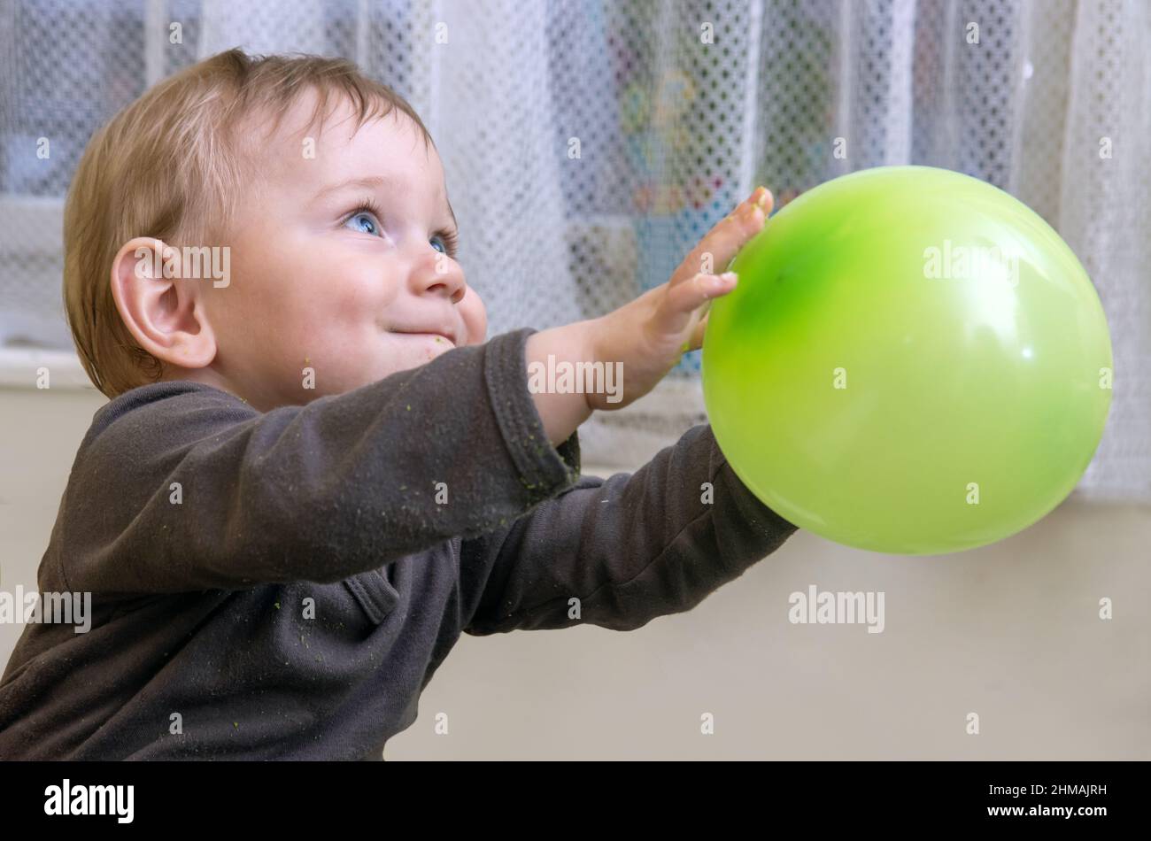 Kleiner Junge mit Krümel auf dem Gesicht und Kleidung wirft einen aufblasbaren Ballon Stockfoto