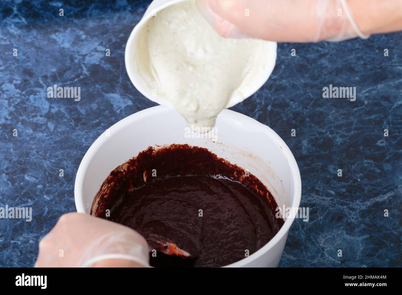 Der Prozess der Herstellung eines Käse-Brownie. Die mit blauem Käse vermischte Creme zur Schokoladenmasse geben. Blauer Marmorhintergrund. Nahaufnahme. Stockfoto