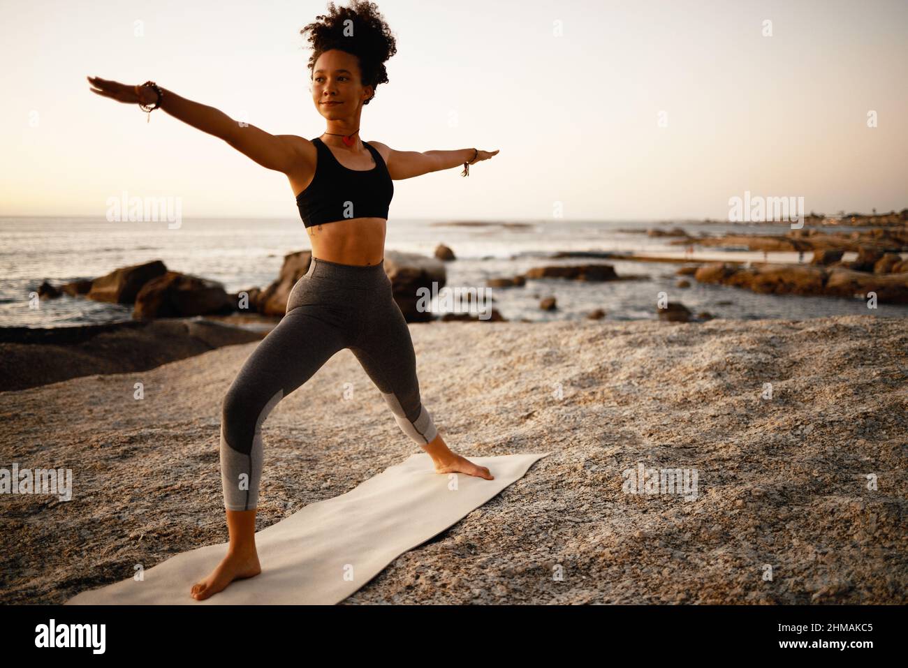 Du kannst deine Ziele durch Yoga erreichen. Ganzkörperaufnahme einer attraktiven jungen Frau, die am Strand bei Sonnenuntergang Yoga praktiziert. Stockfoto