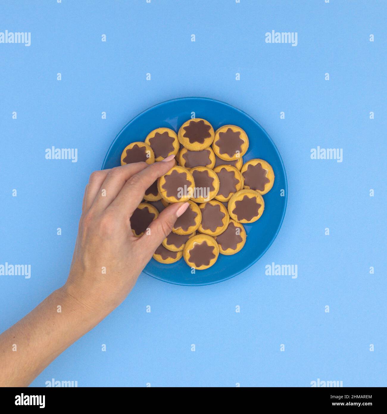 Frau Hand nimmt eine köstliche Schokolade und Keks Cookie von blauen Teller auf cyanfarbenem Hintergrund. Essen flach legen. Stockfoto