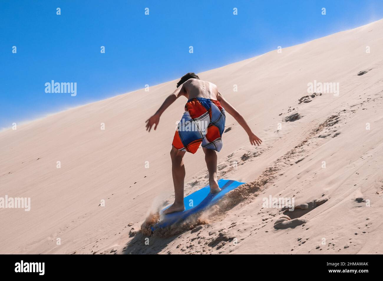 Kaukasischer junger Mann, der auf einem Brett im Sand der Dünen von Tarifa rutscht Stockfoto