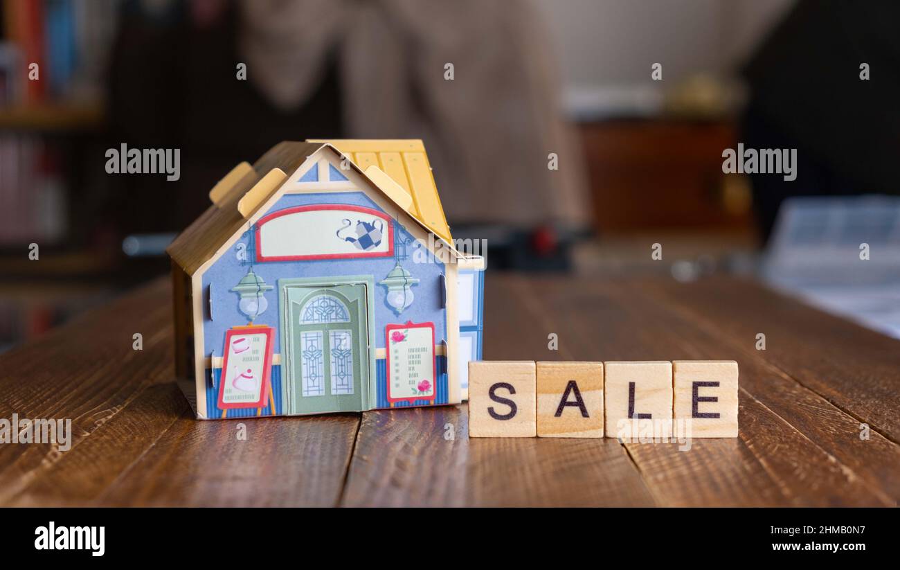 Figur eines Hauses zusammen mit dem Wort Verkauf. Konzept des Eigenheims Verkauf, Immobiliensektor. Stockfoto