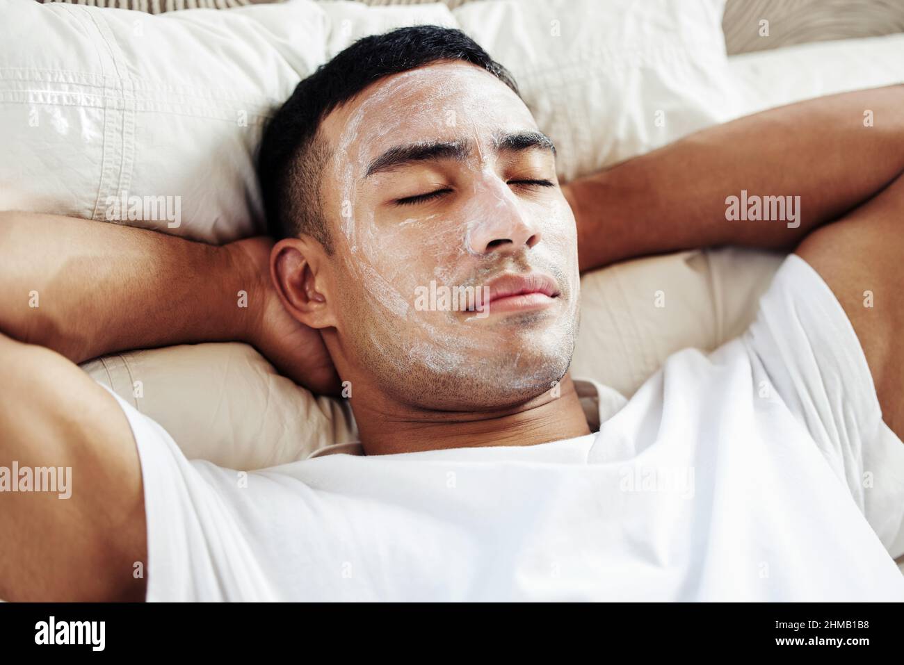 Nehmen Sie sich eine Auszeit für sich selbst, Sie verdienen es. Aufnahme eines Mannes, der eine kosmetische Gesichtsmaske trug, während er zu Hause auf seinem Bett lag. Stockfoto