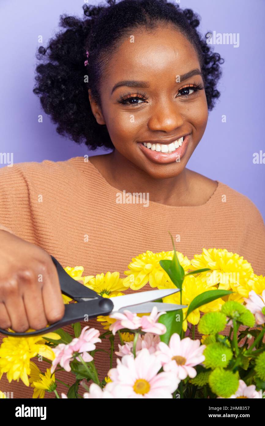Eine junge britische schwarze Frau, die eine Schere über Blumen hält Stockfoto
