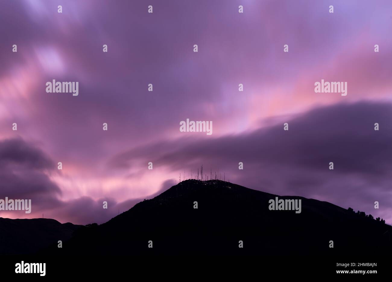 Violetter Sonnenuntergang mit langer Belichtung und Silhouette des Pichincha-Vulkans von der Stadt Quito in Ecuador aus gesehen. Stockfoto