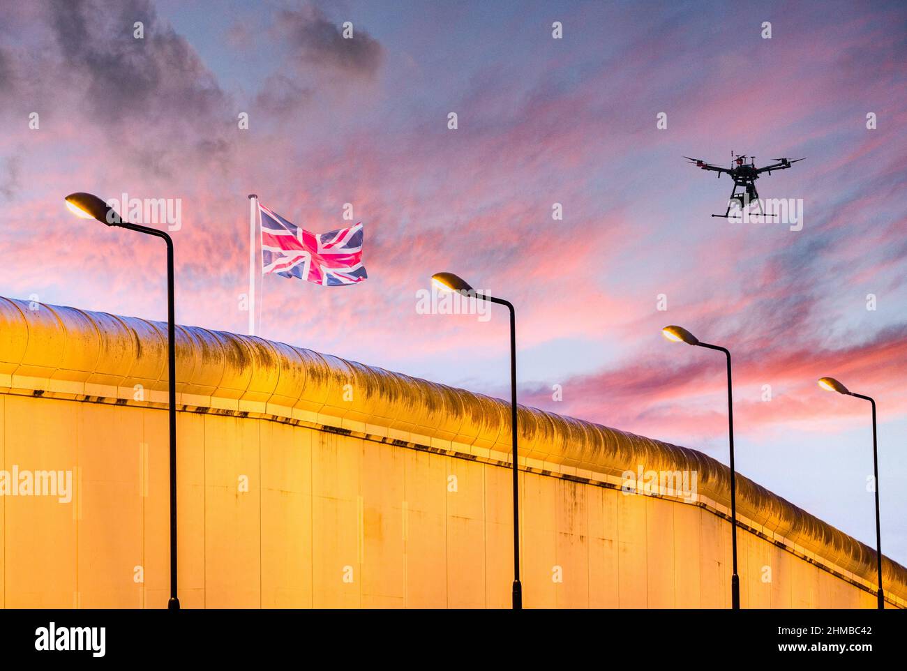 Britische Union Jack-Flagge auf Gefängnis/Grenzmauer mit Drohne am Himmel: Einwanderung, Grenzkontrolle, Brexit, Gefängnisdienst... Konzept Stockfoto