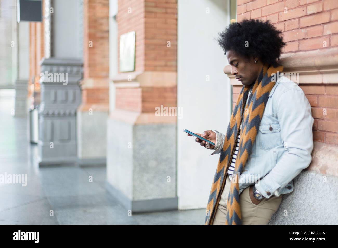 Afroamerikanischer Mann mit Afro-Frisur und lässigem Look mit einem Mobiltelefon an einem öffentlichen Ort. Platz für Text. Stockfoto