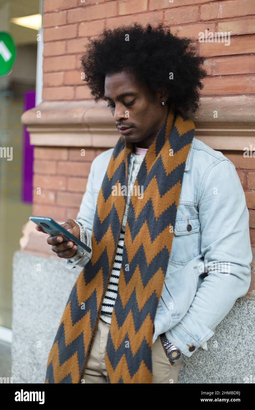 Afroamerikanischer Mann mit Afro-Frisur und modernem Look mit einem Smartphone im Freien. Stockfoto