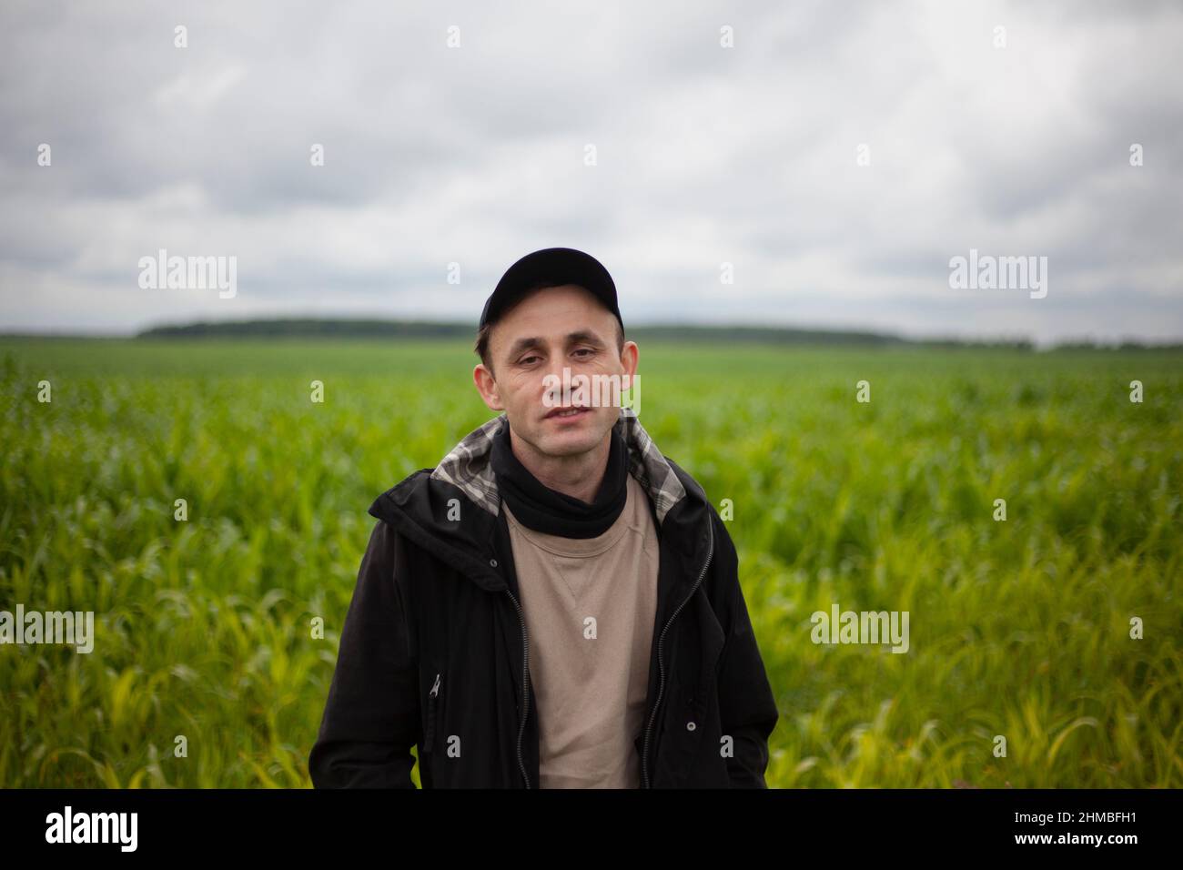 Der Typ steht in einem Kornfeld. Ein Mann in schwarzer Kleidung. Der junge Mann reist. Die Person ist gut gelaunt. Bewölktes Wetter. Stockfoto
