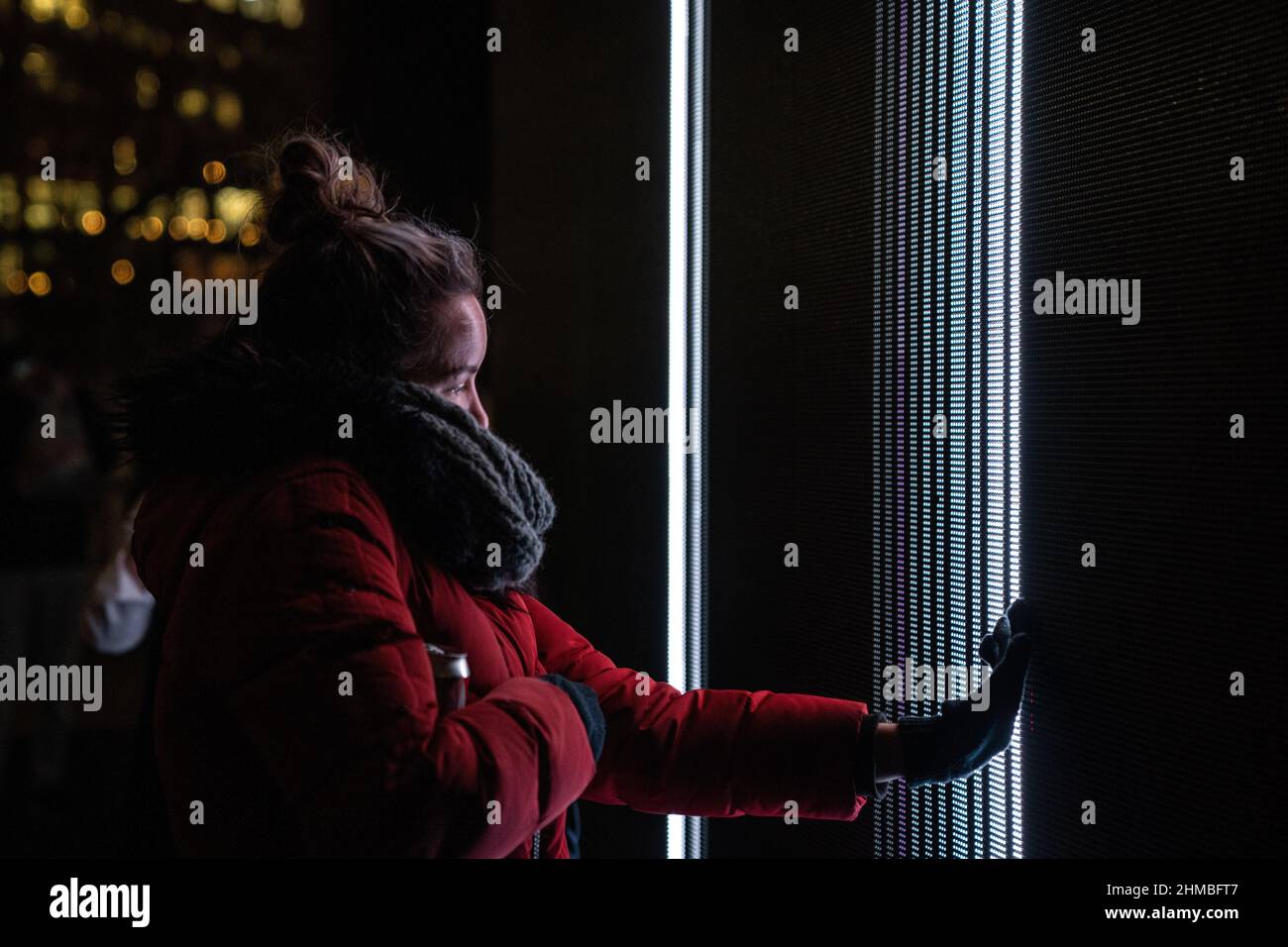 Toronto, Kanada. 07th. Februar 2022. Eine Frau in einem roten Wintermantel nutzt ihre Hand, um mit einer Lichtkunst-Installation ‘Control No Control' von Studio Iregular zu interagieren, einem großen LED-Würfel, der auf alles reagiert, was ihn berührt, und jede Bewegung auf seiner Oberfläche.die Nordic Lights Outdoor-Winterausstellung, Eine Ausstellung nordischer und kanadischer Lichtkunst im Toronto Harbourfront Centre, die gemeinsam mit Fjord Studio produziert wurde. (Foto von Katherine Cheng/SOPA Images/Sipa USA) Quelle: SIPA USA/Alamy Live News Stockfoto